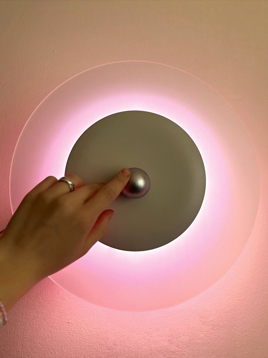 Flux, a circular wall sconce, glowing pink as a hand adjusts it